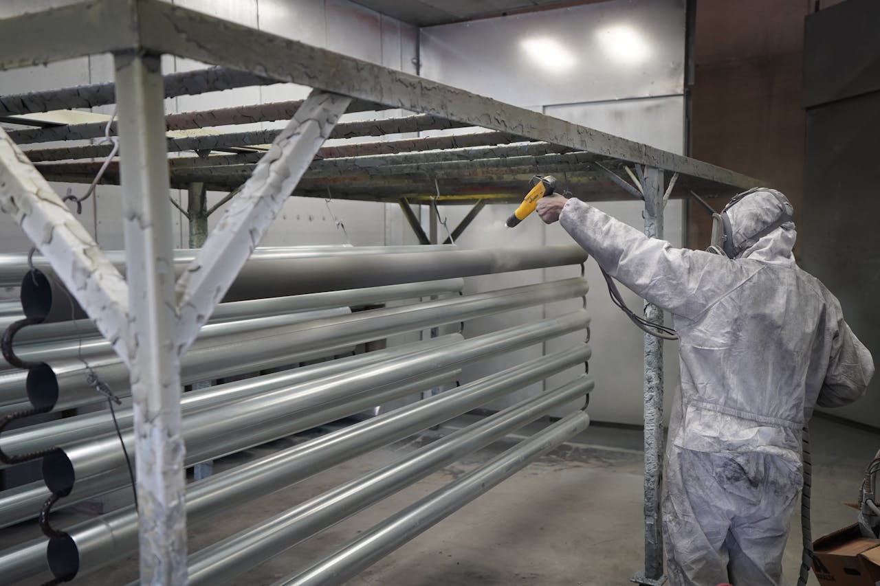 Technician applying powder coating to metal pipes in a workshop setting.