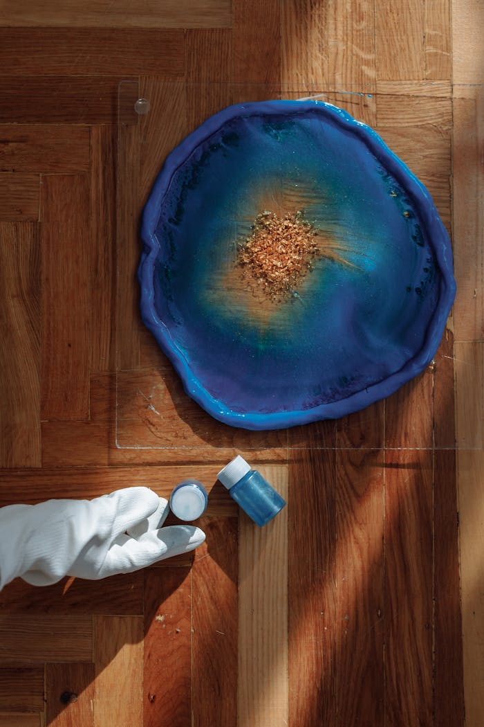 Colorful resin artwork displayed with artist holding pigment jar on wooden floor.